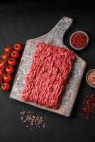 Raw ground beef or pork on a wooden cutting board with spices and salt photo