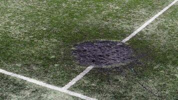 een gat in de grond van een kanon schelp explosie gevulde met vers aarde Bij een Amerikaans voetbal stadion. beschietingen krater in de stad. speelplaats. oorlog in Oekraïne. verwoesting van burger infrastructuur. video