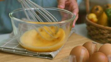 giovane donna cucinando nel luminosa cucina, mani sbattere uova nel un' ciotola posto su asciugamano e di legno tavolo. preparazione ingredienti per salutare cucinando. fatti in casa cibo video