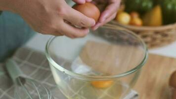 Young woman cooking in a bright kitchen, hand made cracked fresh egg yolks dripping into the bowl. Preparing ingredients for healthy cooking. Homemade food video