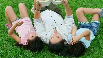 Happy mother and two daughters having fun and enjoying reading at the park. Mother and daughter resting in the summer garden, she reads fairy tales to her daughter. video