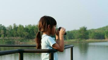 pequeno menina olhando através binóculos às pássaros em a reservatório. explorar e aventura conceito. observação de pássaros video