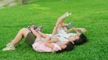 contento madre y dos hijas teniendo divertido y disfrutando leyendo a el parque. madre y hija descansando en el verano jardín, ella lee hada cuentos a su hija. video