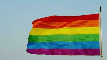 regenboog lgbt vlag fladdert boven de pool in de achtergrond van de blauw lucht. concept van vrijheid en geslacht verscheidenheid video