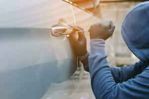 Close up car thief hand holding screwdriver tamper yank and glove black stealing automobile trying door handle to see if vehicle is unlocked  trying to break into inside. photo