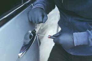 Close up car thief hand holding screwdriver tamper yank and glove black stealing automobile trying door handle to see if vehicle is unlocked  trying to break into inside. photo