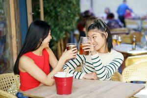 Cheerful Asian friends clinking glasses of drinks in cafe photo