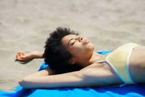 Relaxed ethnic lady sunbathing on sandy shore on summer day photo