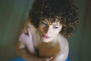High angle of woman with curly hair, with her bare shoulders gazing through the window photo