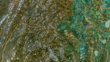 The flow of water runs into a reservoir with a stone bottom, forming a textured surface. video