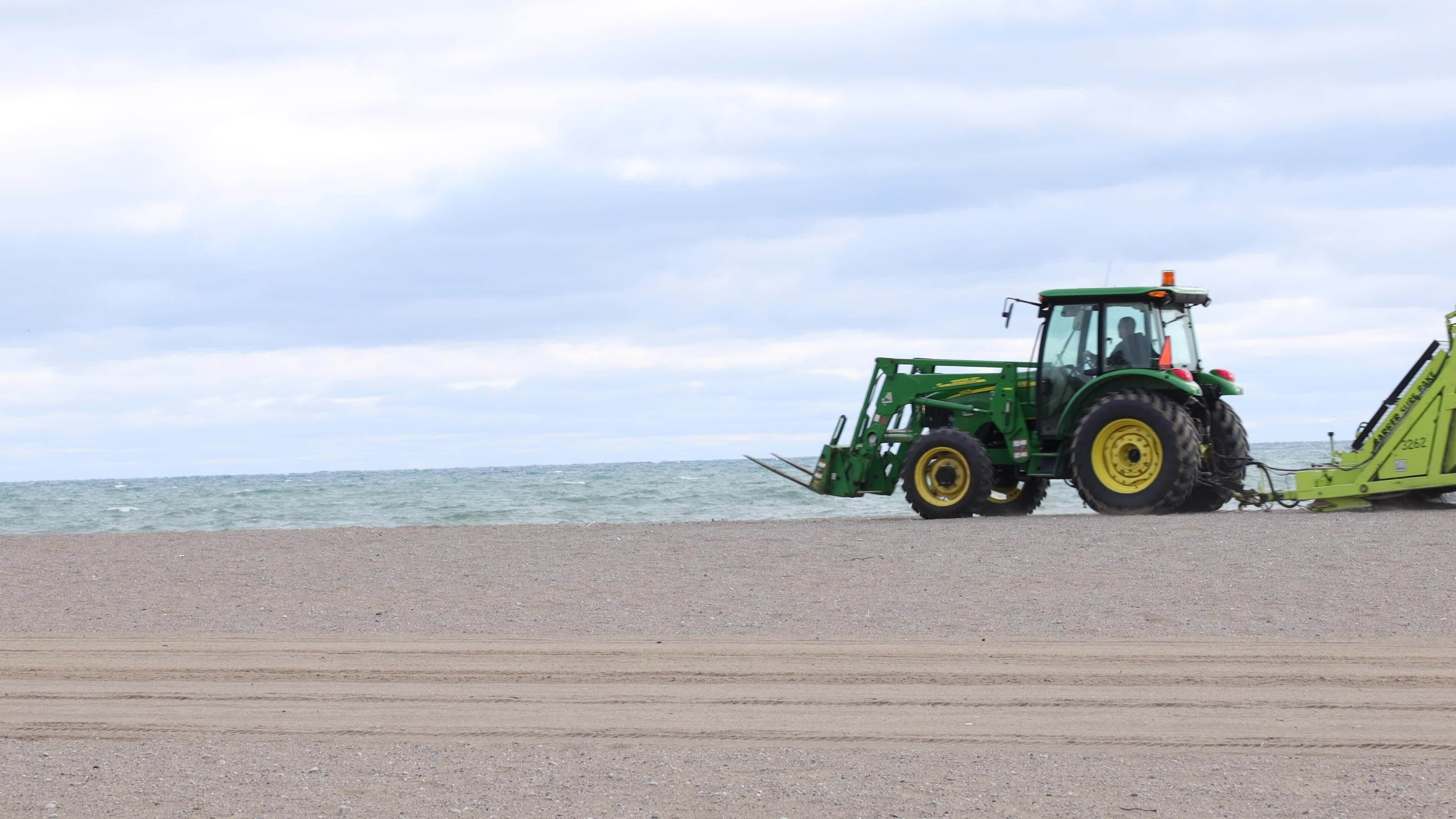 Tractors with pull behind rake grooming and cleaning the beach from rocks  and trash left behind. The beach cleaning machine filters the sand and  leaves a perfectly level and clean waterfront. 24164006