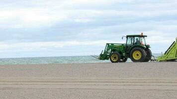 Tractors with pull behind rake grooming and cleaning the beach from rocks and trash left behind. The beach cleaning machine filters the sand and leaves a perfectly level and clean waterfront. video