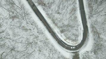 Top down view of hair pin curve going up mountain with snow in Wisconsin. Patterns of fallen branches and undergrowth seen with snow. Lane markings of yellow. video