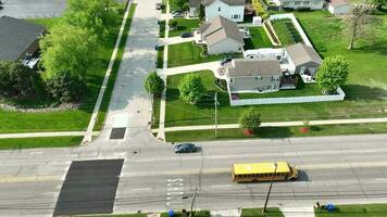 School bus driving down a residential street with school painted on the road from an Aerial view. The road is lined with houses, open green grass areas and trees. video