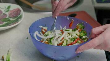 white senior woman stirring vegetable salad in blue bowl with fork, close-up video