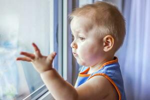 The child looks out the window. He really wants to walk. Because of the quarantine, everyone stays at home and doesn't go anywhere. photo