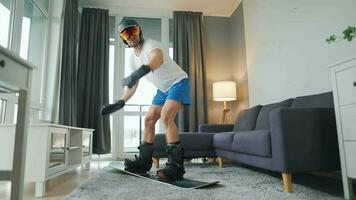 Fun video. Man in shorts and a T-shirt depicts snowboarding on a carpet in a cozy room. Waiting for a snowy winter video