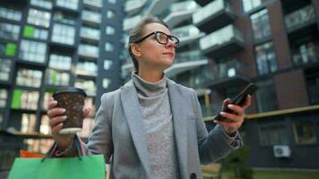 Woman Walking on a Business District Holds Takeaway Coffee Shopping Bags and Uses Smartphone video