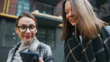 Two happy women walking with takeaway coffee and talking with interest among themselves in the business district. Slow video