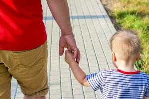 Father and son walk hand in hand. A man leads a child by the hand photo