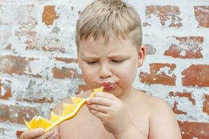 Portrait of child. Cute boy posing and eating a delicious orange. The emotions of a child. photo