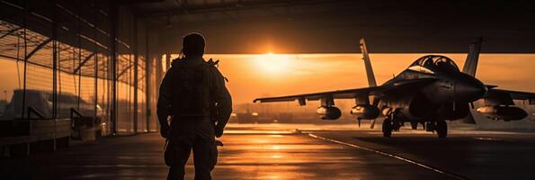Sunset backlit view of military fighter jet pilot beside parked military airforce plane next to barracks or hangar as wide banner with copyspace area for world war conflicts. AI Generative photo