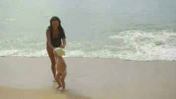 jovem mulher com uma filha de dois anos andando e cantando uma música ao longo da praia, câmera lenta video