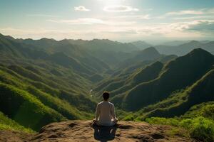 A person meditating on top of a hill, overlooking a vast landscape of mountains and forest. photo