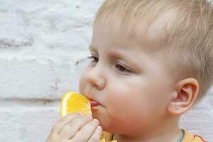 Portrait of child. Cute boy posing and eating a delicious orange. The emotions of a child. photo