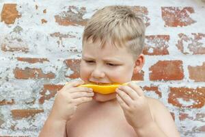 Portrait of child. Cute boy posing and eating a delicious orange. The emotions of a child. photo