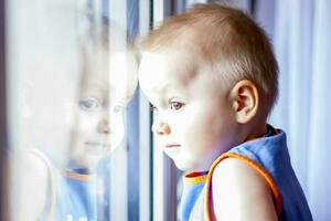The child looks out the window. He really wants to walk. Because of the quarantine, everyone stays at home and doesn't go anywhere. photo