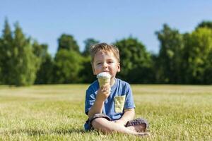 A happy boy is eating ice cream outdoors in the park. photo