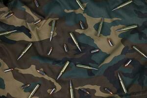 Many rifle bullets and cartridges on dark camouflage background photo