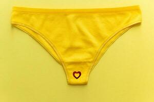 Top view of colorful females panties with red heart confetti on  yellow background, close up. photo