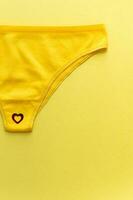 Top view of colorful females panties with red heart confetti on  yellow background, close up. photo