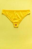 Top view of colorful females panties with red heart confetti on  yellow background, close up. photo