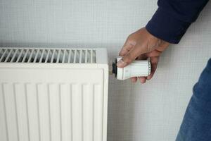 Cropped view of men hand adjusts temperature of central heating radiator, photo