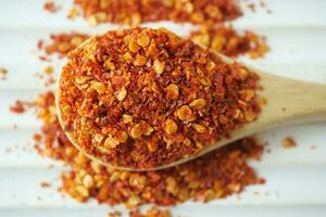 top view of chili flakes on wooden spoon on white photo