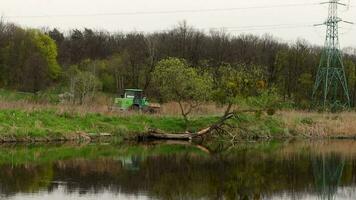 le tracteur monte le long de le banque de une rivière ou Lac dans le forêt. video