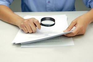 Focus magnifying glass, Hand of businessperson looking at documents through magnifying glass. Concept of business and data validation. photo