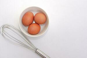 Top view of chickken eggs in a bowl and egg whisks on white background. Copy space. photo
