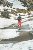 un hombre atleta carreras en un la carretera mediante un alpino pasar foto