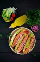 Hot dog with  sausage, pickled cucumber, tomatoes, red onions and lettuce on dark wooden background. Summer hotdog. Top view photo