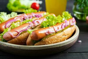 Hot dog with  sausage, pickled cucumber, tomatoes, red onions and lettuce on dark wooden background. Summer hotdog. photo