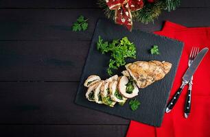 Roasted sliced Christmas roll of turkey with spinach and cheese on dark rustic background. Top view, copy space. Festival food. photo