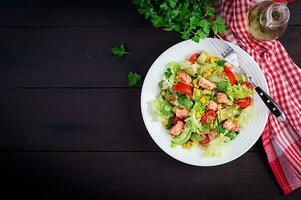 Salad with grilled salmon, lettuce, avocado, tomatoes and corn on a white bowl. Paleo diet. Top view, copy space photo