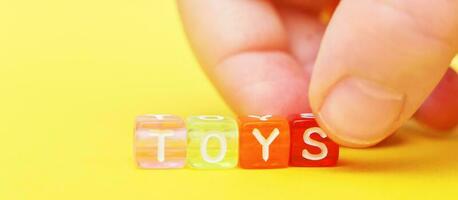 Word toys with colorful cubes of beads and child's hand on yellow background. banner photo