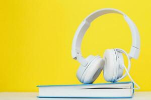 concepto de libro de audio con auriculares blancos modernos y libro de tapa dura sobre un fondo amarillo. escuchando un libro. foto