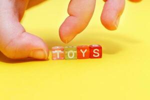 Word toys with colorful cubes of beads and child's hand on yellow background photo