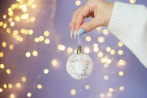 womans hands with nails holding christmas toy ball on a purple festive blurred bokeh background photo